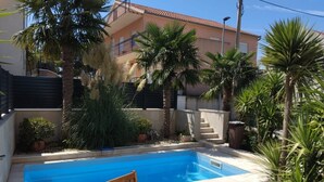 A swimming pool with a wooden chair, surrounded by palm trees and potted plants. - Villa Marija - Five Bedroom Villa with Terrace and Swimming Pool (Podstrana)
