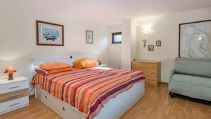 Un dormitorio con cama, mesitas de noche, cómoda, una silla e iluminación en la pared.