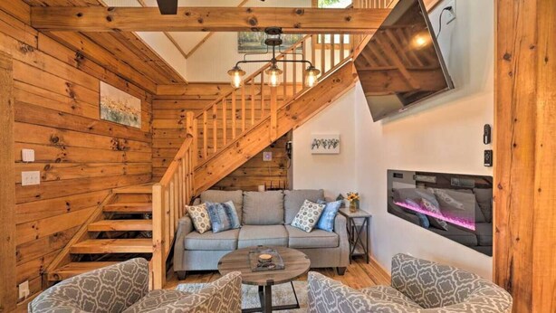 L’intérieur d’un chalet chaleureux, avec un escalier en bois, un ensemble de canapés et un téléviseur fixé au mur.