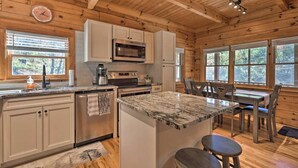 Une cuisine avec des murs en bois, un plan de travail en granit, un îlot central et un coin repas avec une table et des chaises.