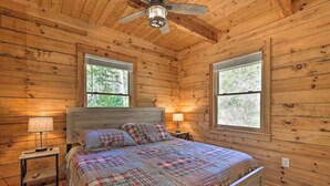 Une chambre dans une cabane en bois, avec un lit, deux lampes de chevet et un ventilateur de plafond.