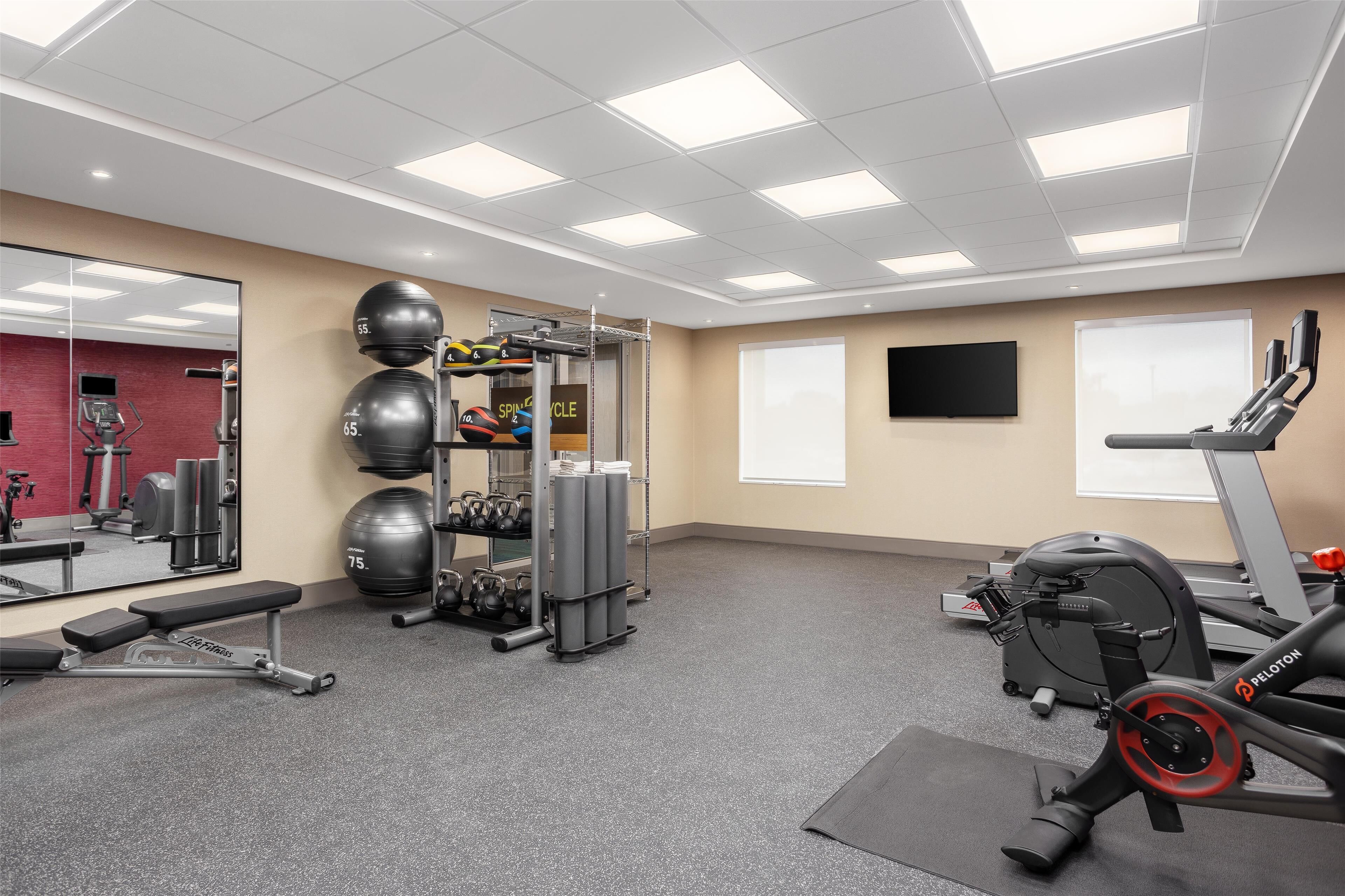 Et fitnessrum med træningsudstyr, en bænk, et løbebånd og en spejlvæg.