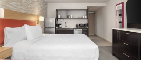 A hotel room with a large bed, a kitchenette, a flat-screen TV, and a mirror.