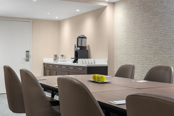 A conference room with a long table, six chairs, and a coffee machine.