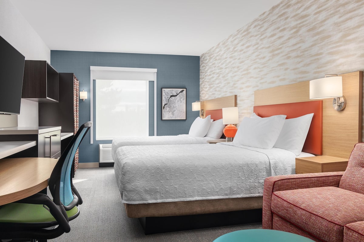 A hotel room with a bed, desk, chair, and a large window.