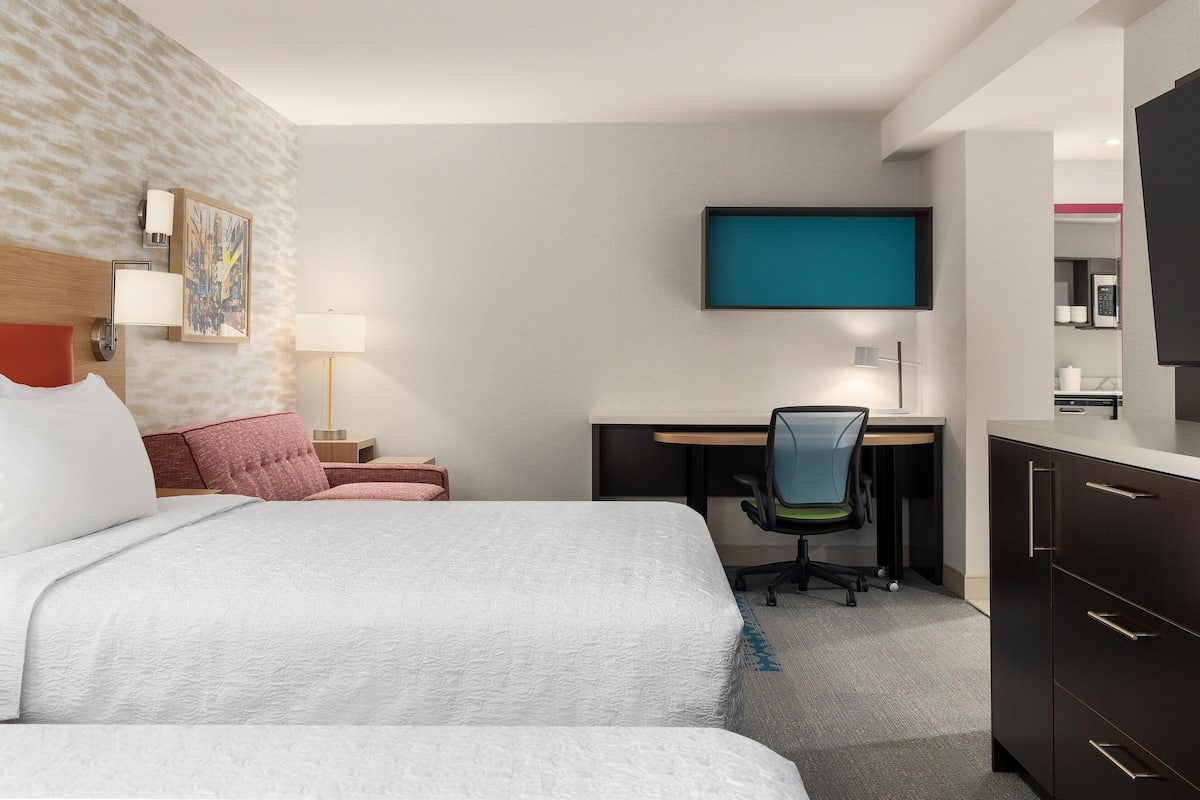 A hotel room with a bed, desk, chair, and a flat-screen TV mounted on the wall.