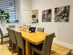 Uma área de refeições com mesa de madeira, seis cadeiras e objetos decorativos, incluindo flores e uma garrafa de champanhe.