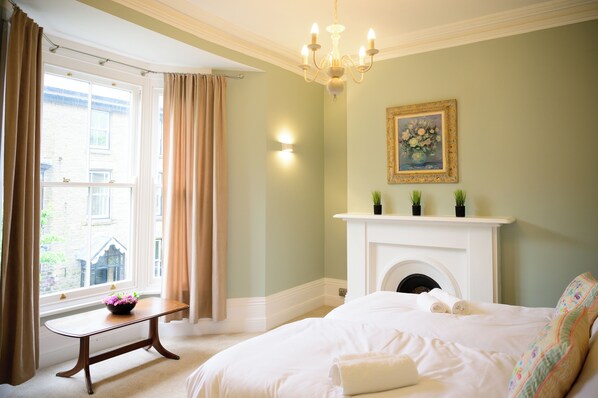 Une chambre à coucher avec un lit, une cheminée, une fenêtre avec des rideaux et un lustre.