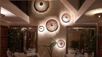 An outdoor dining area with white metal chairs and tables, a central potted plant, and decorative wall sconces.