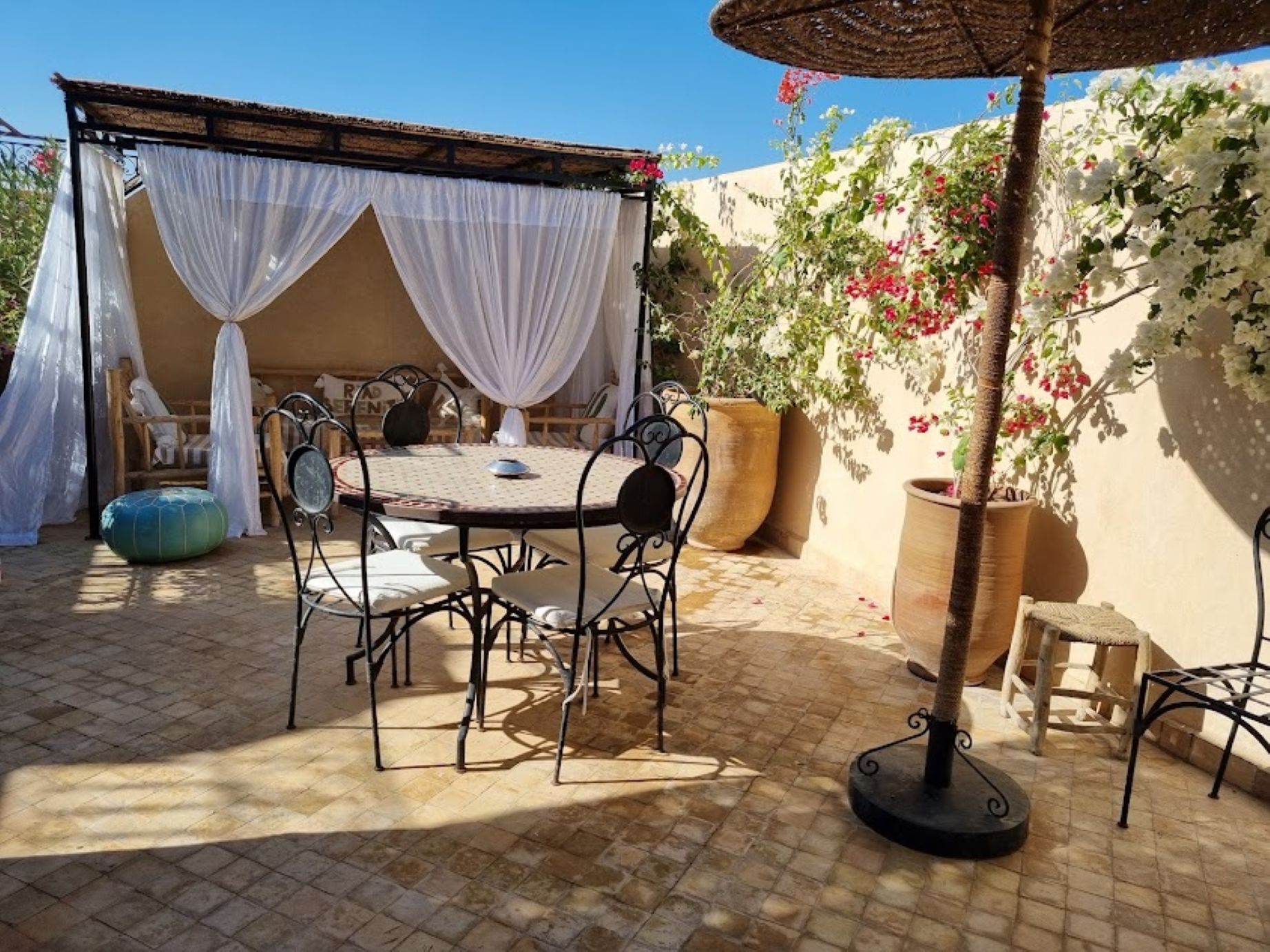 A patio with a round table and chairs, a pergola with white drapes, and potted plants.