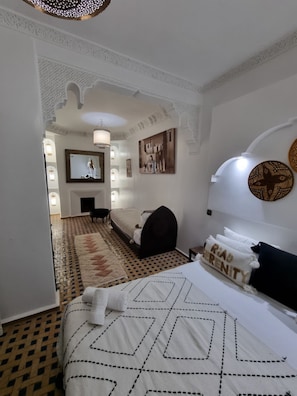 A hotel room with a bed, a TV, a wall-mounted lamp, and a patterned rug. - Riad Dar Serenity (Marrakech)
