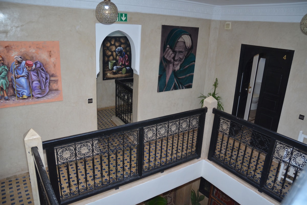 Una escala amb baranes negres ornamentades i una paret amb dos quadres.
