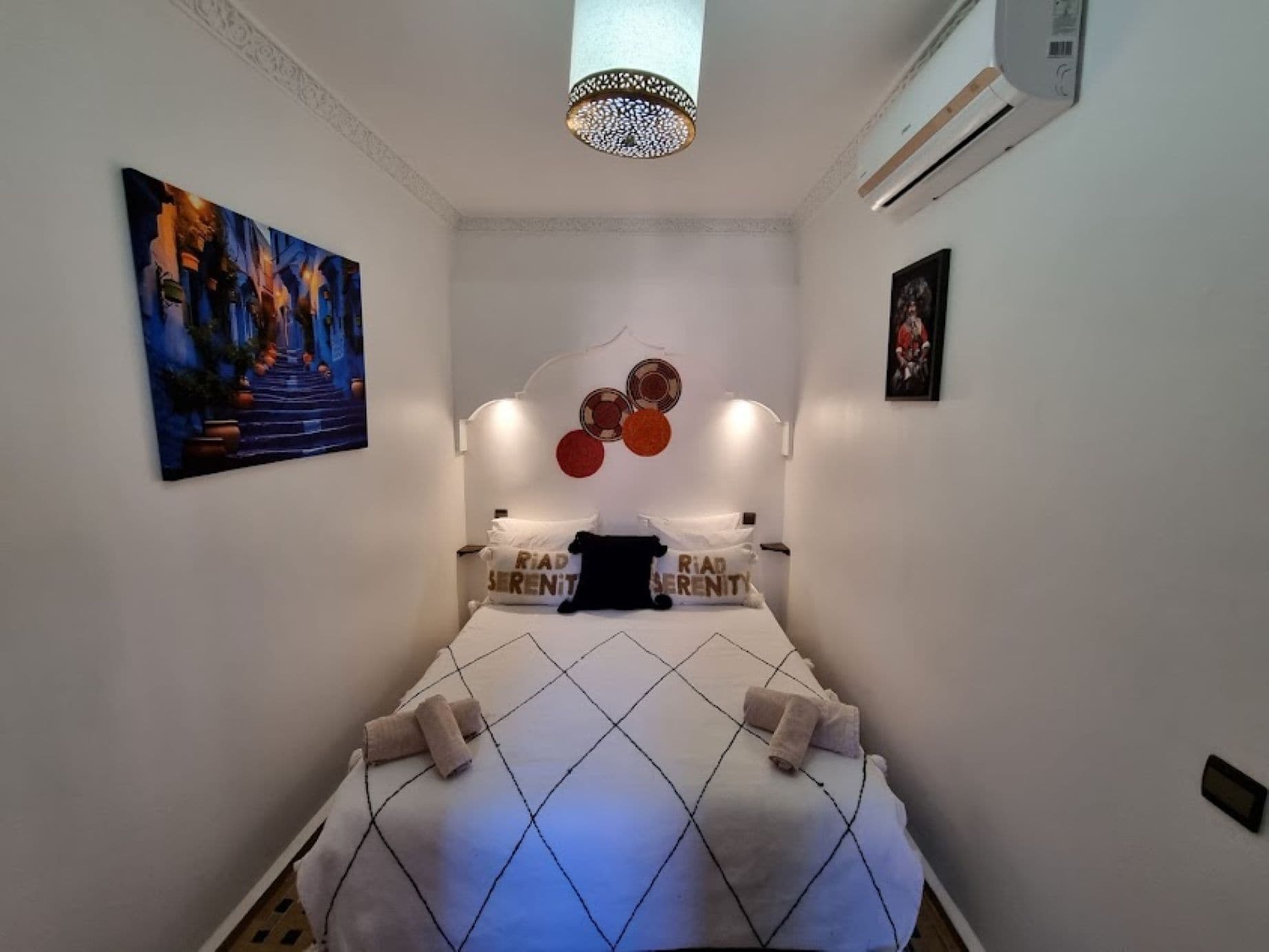A bedroom with a bed, a painting, a ceiling light fixture, and an air conditioning unit.