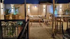 An outdoor patio area with a wooden table and chairs, potted plants, and wall-mounted lighting. - Riad Dar Serenity (Marrakech)