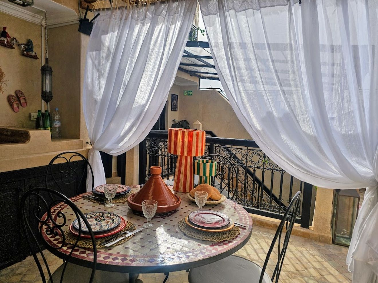 A round table with a Moroccan-style tablecloth, surrounded by chairs, and a decorative vase.