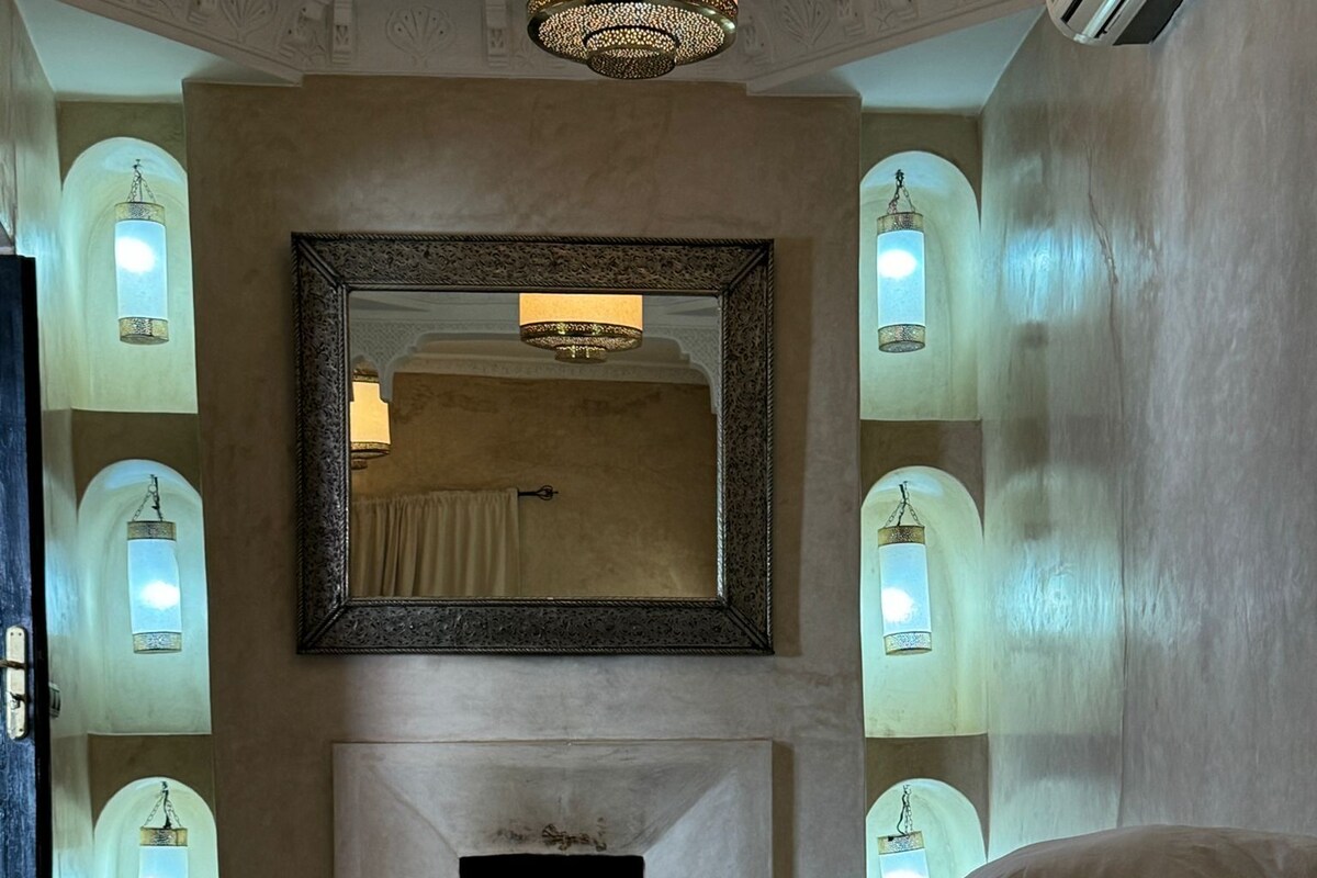 A bedroom with a large bed, a fireplace, and wall-mounted sconces.