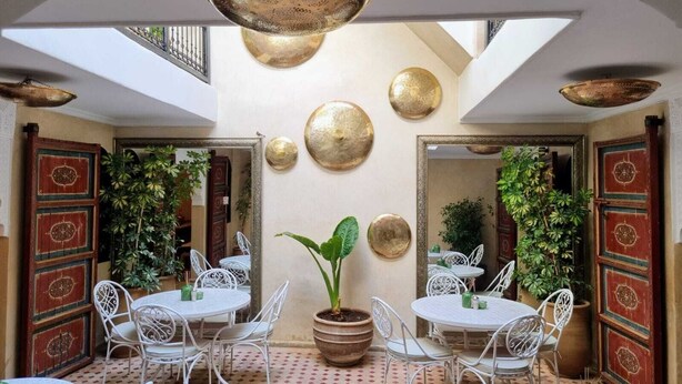 A dining area with round tables and white chairs, surrounded by decorative plates and a large potted plant. - Riad Dar Serenity (Marrakech)