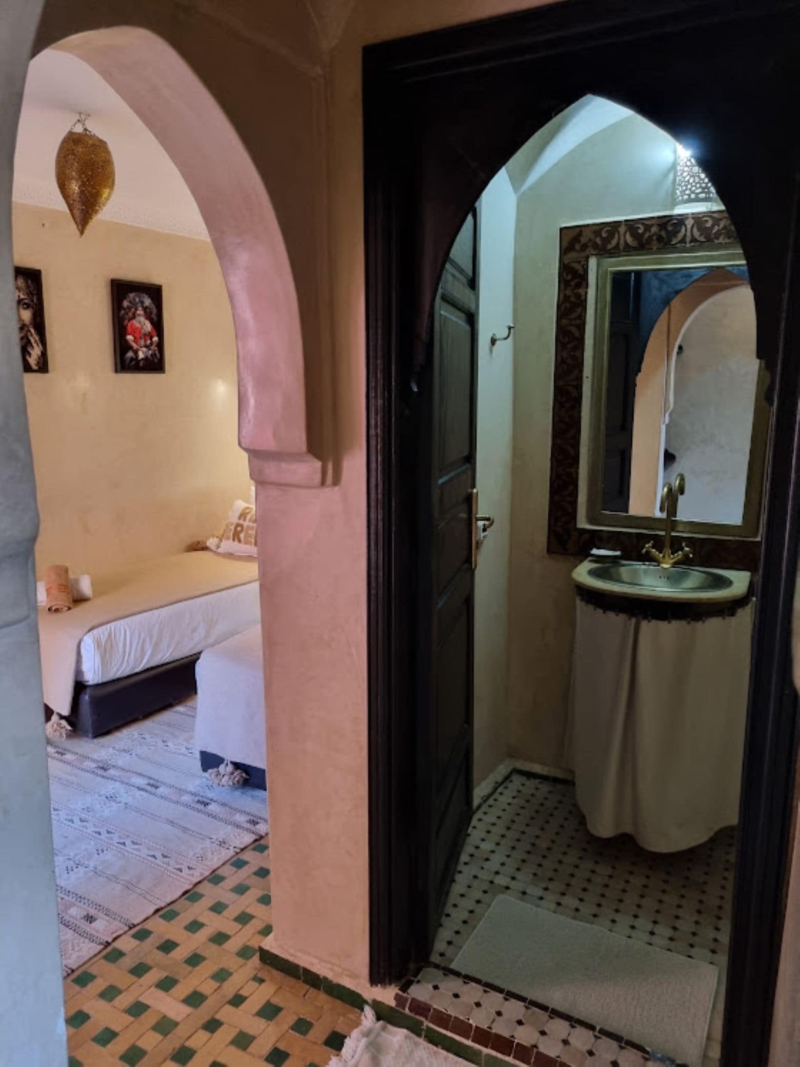 Een kamer met een bed, een badkamer met een wastafel en spiegel, en een vloer met een patroon.