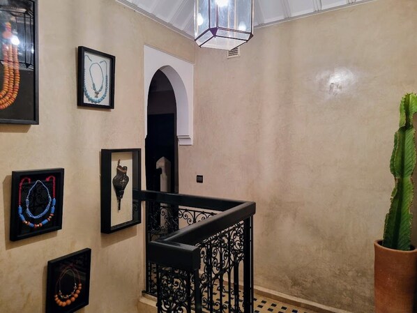 A staircase with ornate black railings, a framed picture of a necklace, and a potted plant. - Riad Dar Serenity (Marrakech)