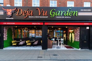A restaurant named Deja Vu Garden with a bar and restaurant sign, outdoor seating, and a brick building in the background. - Charming London Apartment Near Attractions (London)