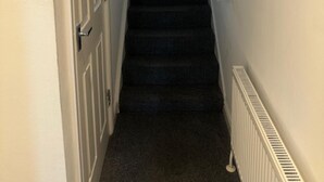 Un corridoio stretto con una scala rivestita di moquette che conduce a una porta in fondo.