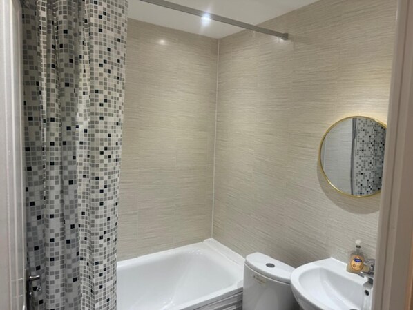 A bathroom with a shower, a bathtub, a toilet, and a sink. - Lewisham Apartment Escape (London)