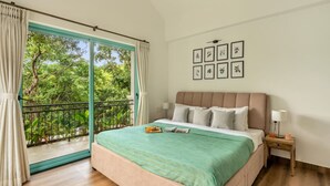 A bedroom with a large window, a bed with a green bedspread, a nightstand with a lamp, and framed pictures on the wall. - 3bhk Villa w Private Pool Assagao Villa C Leste (Parra)