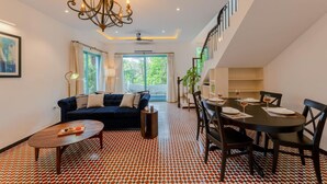 A modern living room with a dark blue sofa, a wooden coffee table, and a dining area with a black table and chairs. - 3bhk Villa w Private Pool Assagao Villa C Leste (Parra)