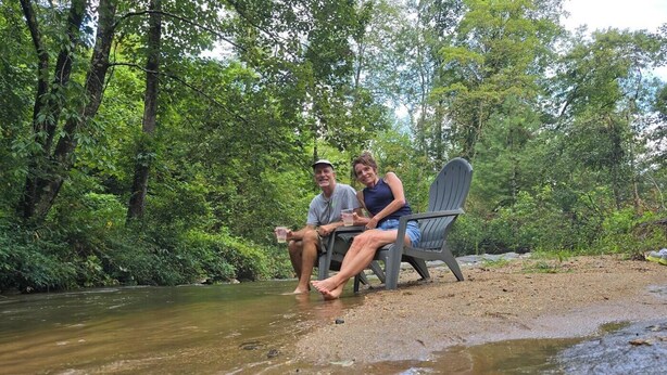Two people relaxing by a creek in a natural setting. - Cozy Warm Creekside Escape w/ WiFi & Hot Shower (Purlear)