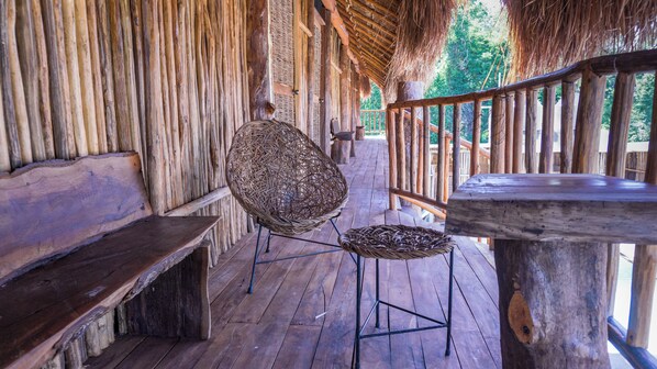 A wooden deck with a woven chair and bench, surrounded by wooden railings and a thatched roof. - Jungla & Estrellas (Coba)