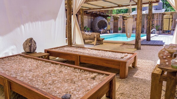 A spa area with wooden tubs filled with salt, a hanging hammock, and a pool in the background. - Jungla & Estrellas (Coba)