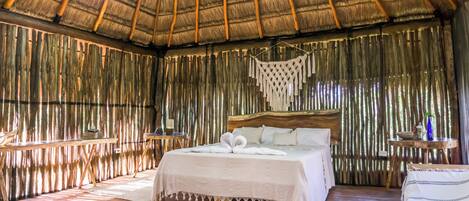 A room with a bed, wooden floors, a ceiling fan, and a thatched roof.
