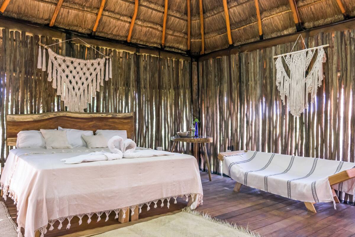 A room with a bed, a daybed, and a small table with a plant.