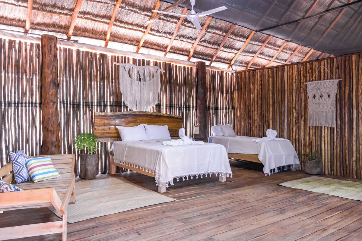A rustic room with two beds, wooden floors, and a thatched roof.