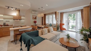 Une cuisine moderne avec un coin repas, un salon avec un canapé et une table basse, et une grande fenêtre avec des rideaux.