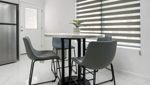 Une cuisine moderne avec un réfrigérateur en acier inoxydable, une porte blanche et un coin repas comprenant une table ronde et quatre chaises.
