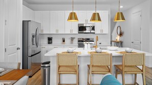 Une cuisine moderne avec des meubles blancs, des appareils en acier inoxydable et un îlot central doté de tabourets de bar.