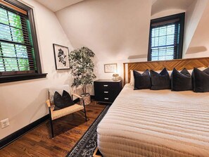 Quarto com cama, mesa de cabeceira, cadeira, planta em vaso e janela.