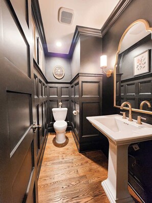 A modern bathroom with dark wood paneling, a white toilet, a vanity with a sink, and a mirror.
