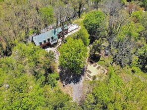 An aerial view of a property with a main building, a large tree, and a separate structure with a covered patio.