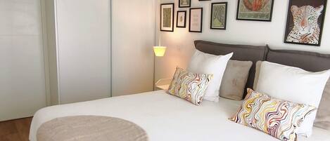 Ein Schlafzimmer mit einem großen Bett, einem Nachttisch, einer Lampe und gerahmten Kunstwerken an der Wand.