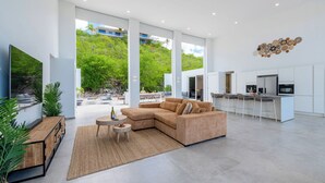 Ein modernes Wohnzimmer mit einer Eckcouch, einem kleinen runden Tisch und einer Küchenzeile mit Barhocker.