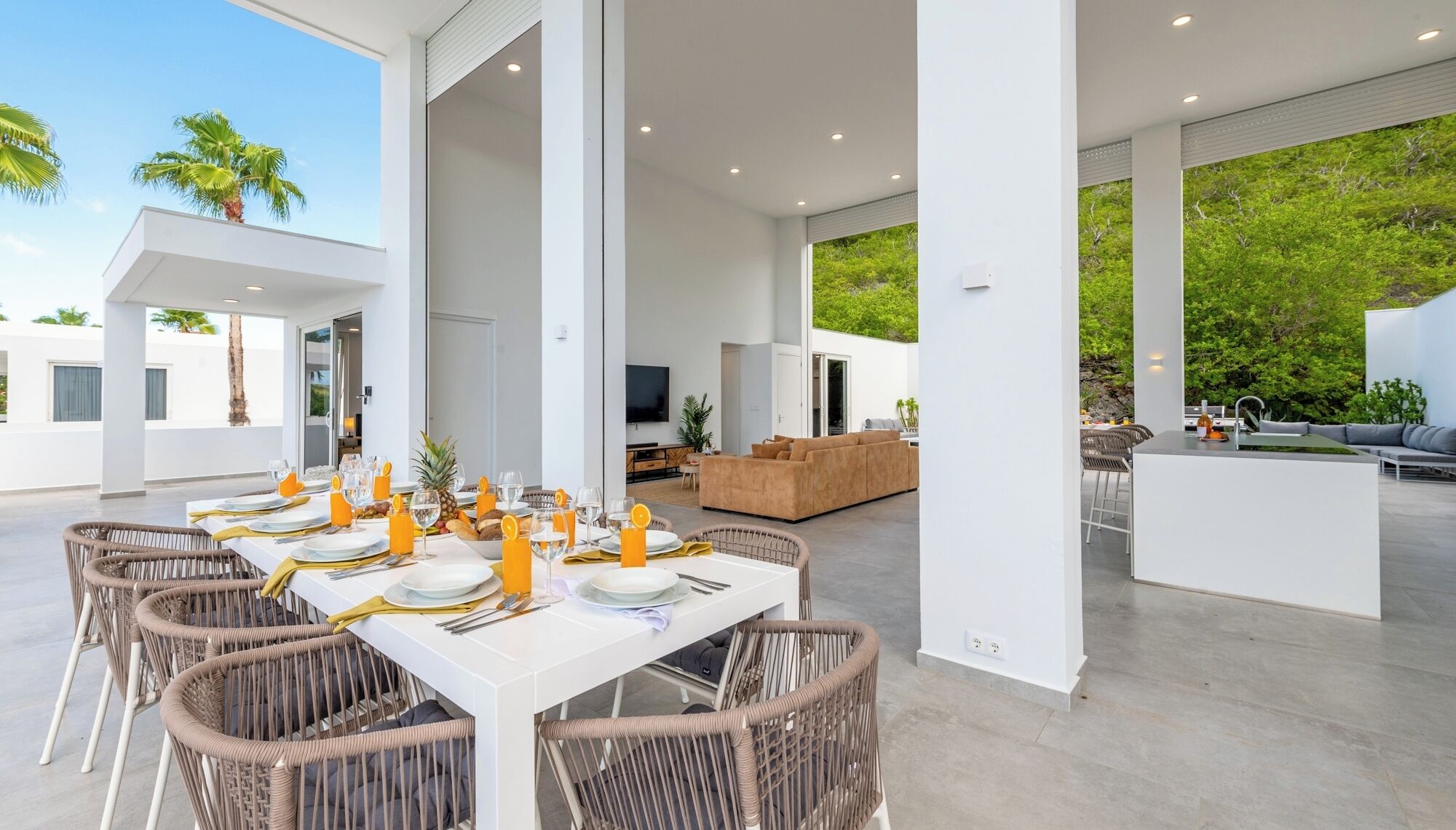A spacious outdoor dining area with a long table set for a meal, surrounded by wicker chairs.