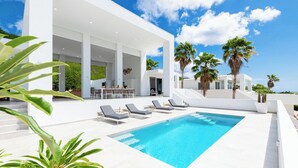 Ein moderner Poolbereich mit rechteckigem Pool, Liegestühlen und Palmen.