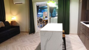 Un saló modern amb un dibuix de sòl en espiga, una illa central amb encimera de marbre blanc, i una zona de menjador amb mobles de fusta.