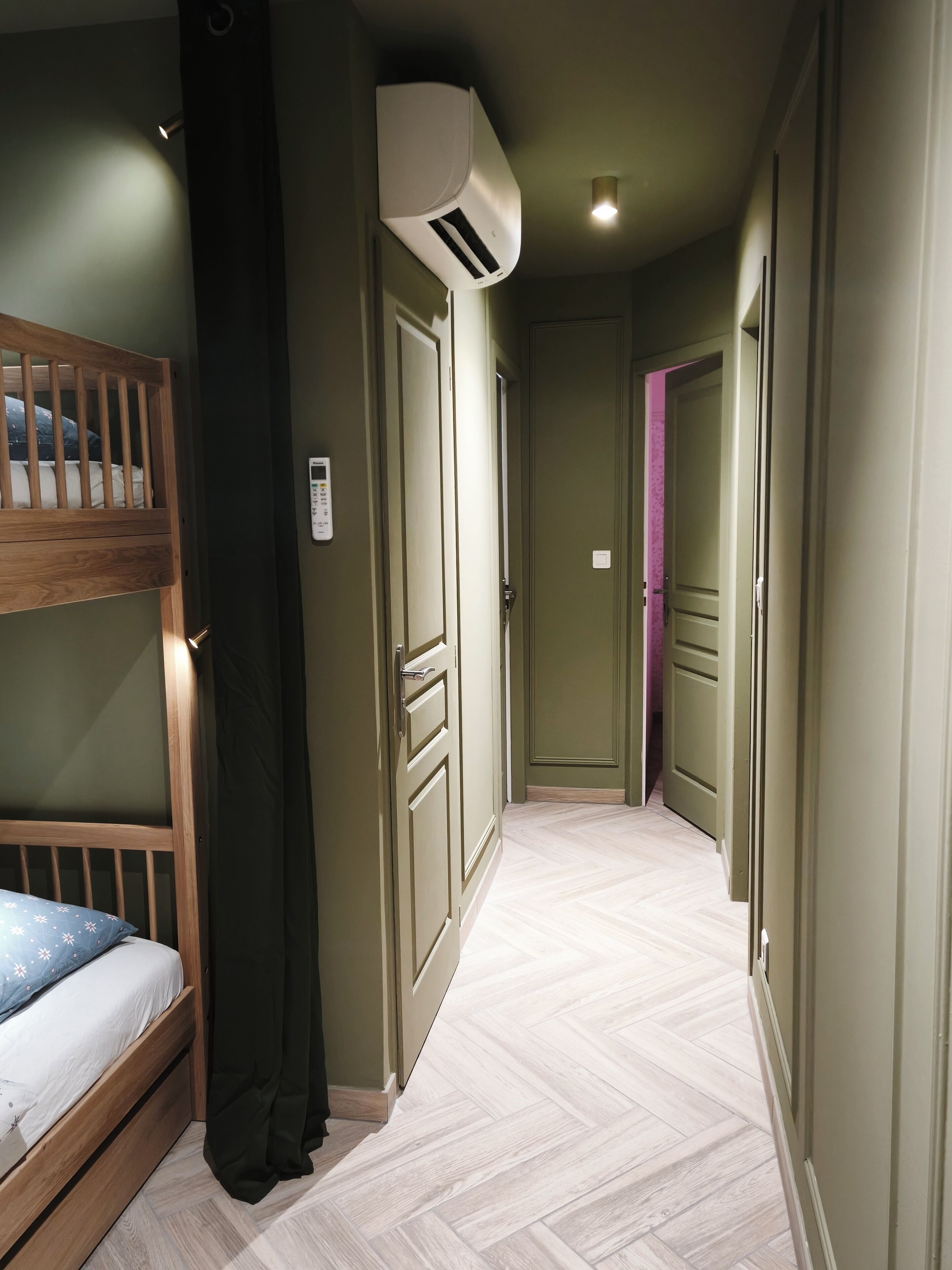 A narrow hallway with a bunk bed on the left, a door with a purple accent, and an air conditioning unit mounted on the wall.