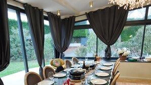 Una sala menjador amb una taula gran ben a punt per a sis persones, envoltada de cadires, amb vista a vegetació a l'exterior.