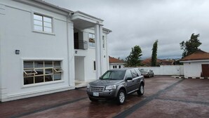 Een wit gebouw met een garage, een overdekte veranda en een auto ervoor geparkeerd.