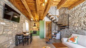 A rustic interior with stone walls, a wooden ceiling, a staircase, a dining area, and a sofa with a colorful pillow. - Holiday house RURAL HOME FRANE (Kornić)