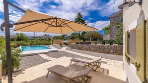 A pool area with lounge chairs and a table, surrounded by stone walls and potted plants. - Holiday house RURAL HOME FRANE (Kornić)